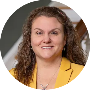 Professional headshot: smiling woman with curly hair in a yellow blazer indoors, suitable for a business profile.