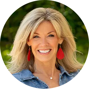 Smiling blonde woman wearing a denim jacket and red tassel earrings outdoors.